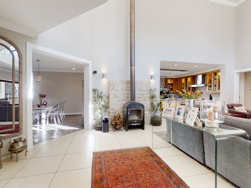 Spacious open-plan living area featuring a striking freestanding fireplace with stone surround, high vaulted ceilings, and neutral tiled flooring throughout.