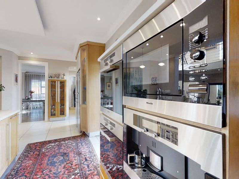 Modern kitchen featuring high-end integrated Miele appliances, timber cabinetry, stone countertops, and recessed lighting, offering a functional and well-maintained culinary space.