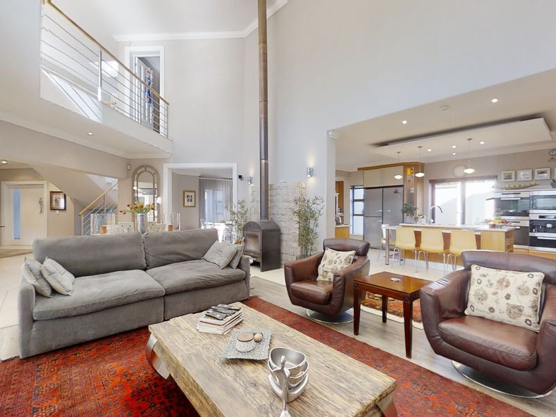 Spacious open-plan living area featuring a double-volume ceiling, a central freestanding fireplace, and a modern kitchen with an island and integrated appliances.