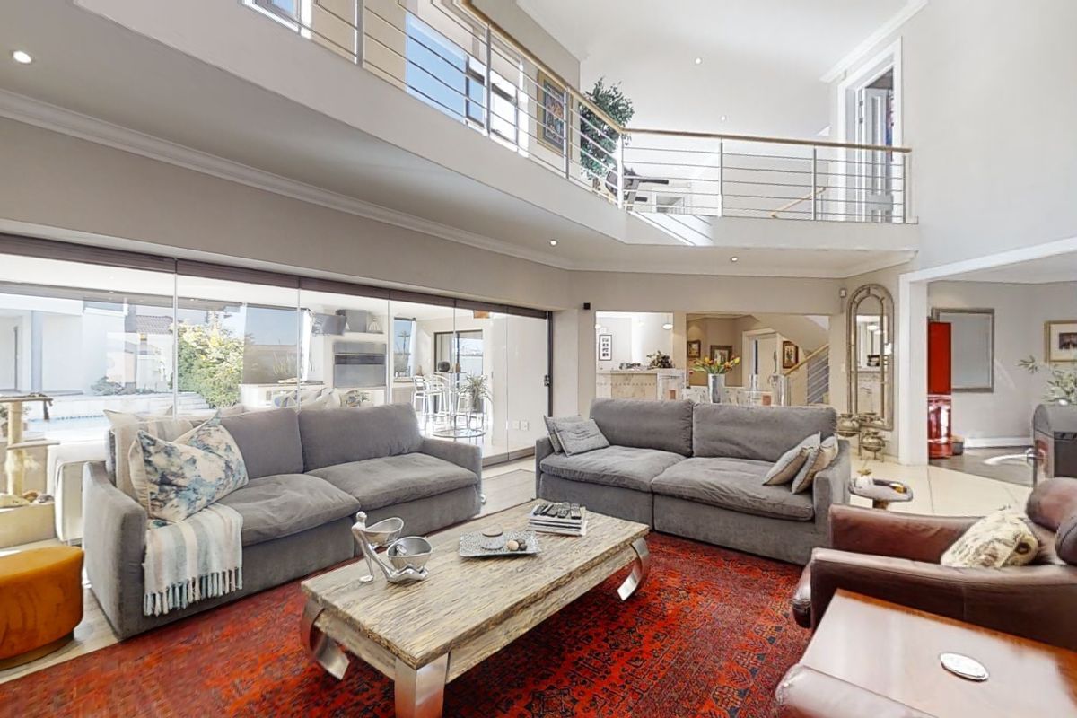 Spacious double-volume living room featuring a mezzanine level, stainless steel balustrades, a modern freestanding fireplace, and large sliding doors opening to the outdoor area.