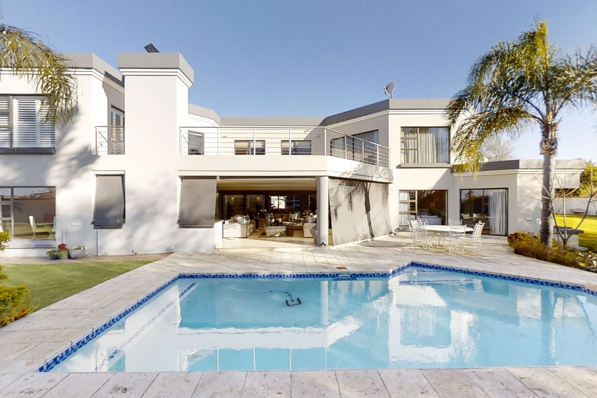 Rear elevation of a modern two-story house featuring a swimming pool, paved patio area, and an upper-level balcony with stainless steel railings.
