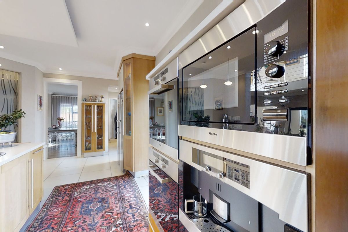 Modern kitchen featuring high-end integrated Miele appliances, timber cabinetry, stone countertops, and recessed lighting, offering a functional and well-maintained culinary space.