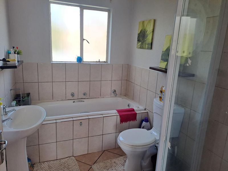 A functional bathroom featuring a pedestal basin, built-in bathtub, separate shower enclosure, and neutral ceramic tiling throughout.