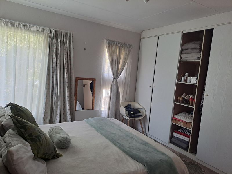 A bedroom featuring built-in cupboards with shelving and large windows allowing natural light.