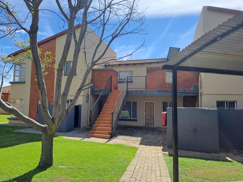 Rear view of the apartment complex featuring a paved courtyard, external staircase access to the upper level, and established garden area.