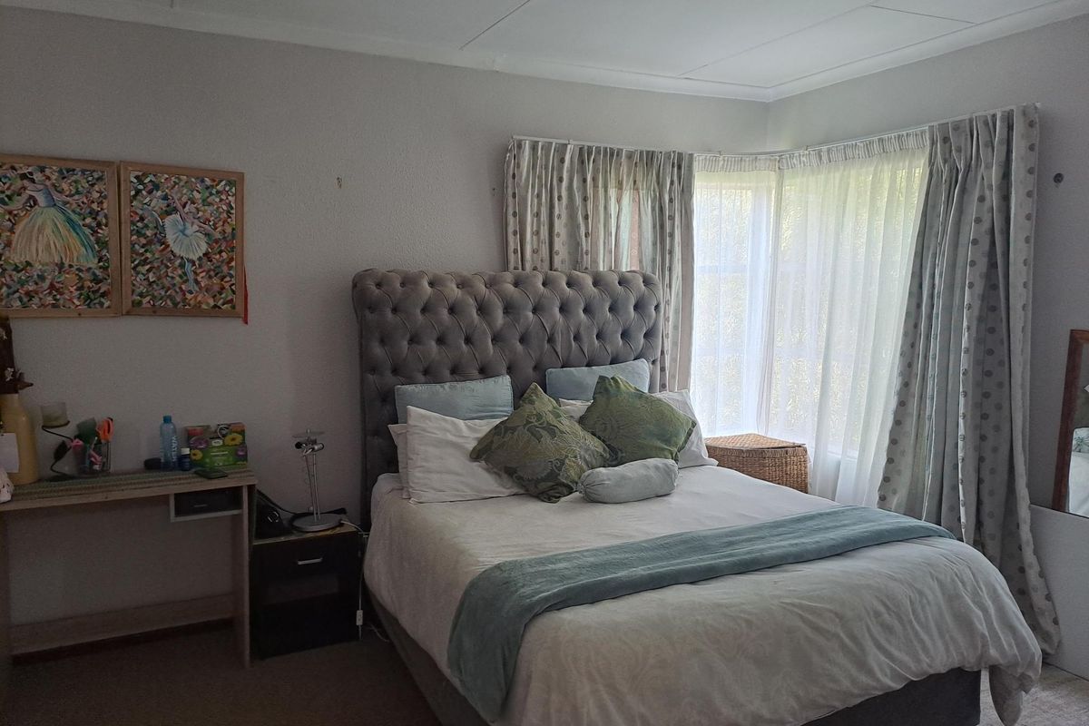 A comfortable bedroom featuring a large bay window with fitted curtains, providing natural light and a classic layout.