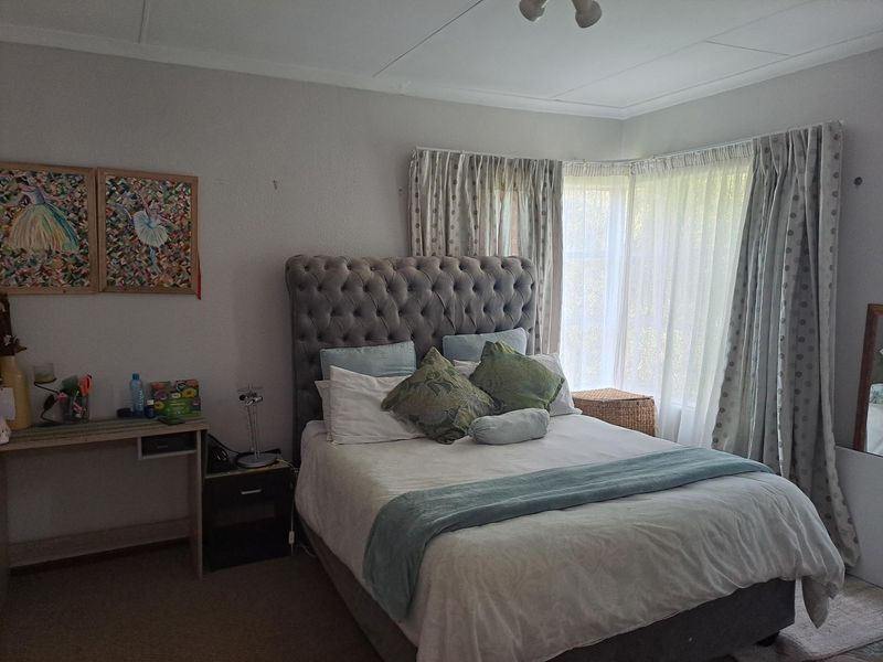 A comfortable bedroom featuring a large bay window with fitted curtains, providing natural light and a classic layout.