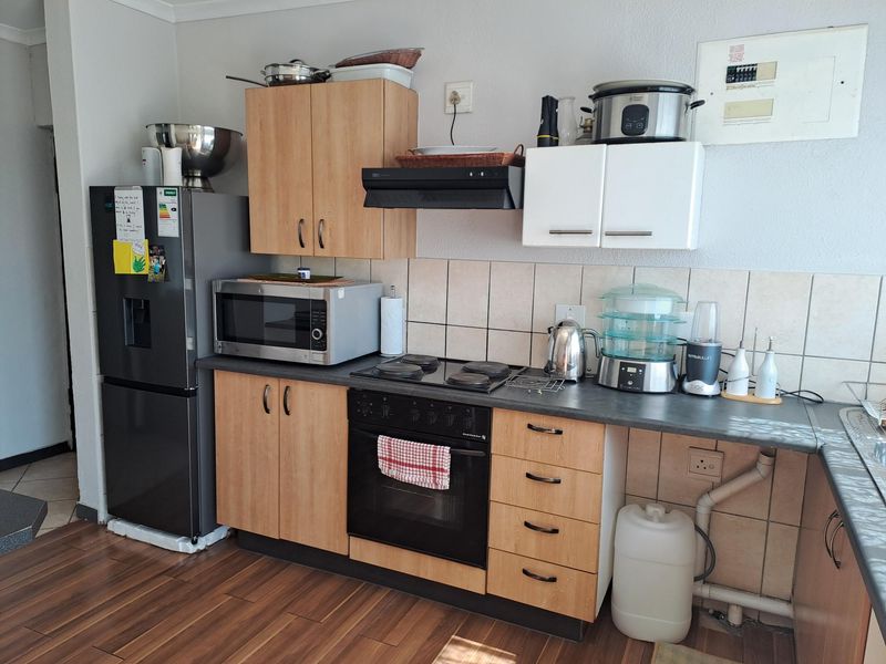 A functional kitchen featuring laminate cabinetry, a built-in oven with electric hob, extractor fan, and tiled backsplash with visible plumbing infrastructure.