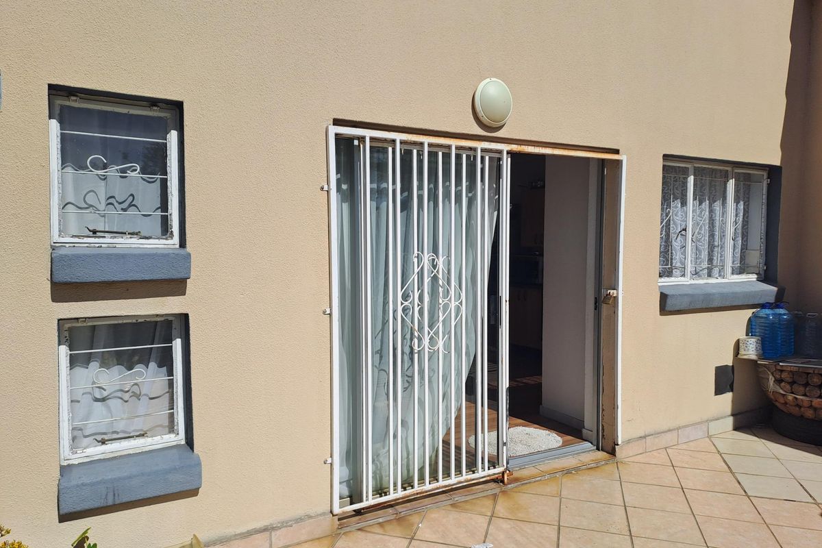 Rear exterior view of the apartment featuring a tiled patio, security gate, and window security bars.