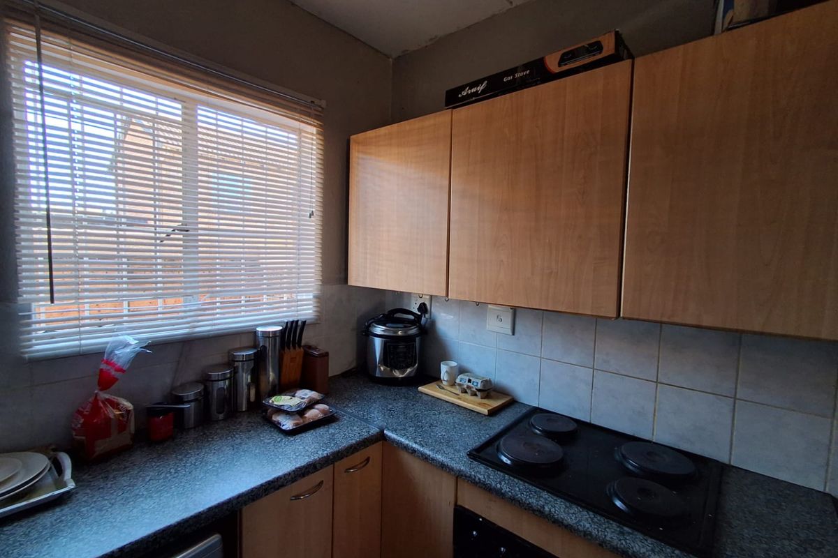 A functional kitchen area featuring light wood-tone cabinetry, dark laminate countertops, a built-in electric hob, and a window with fitted blinds.