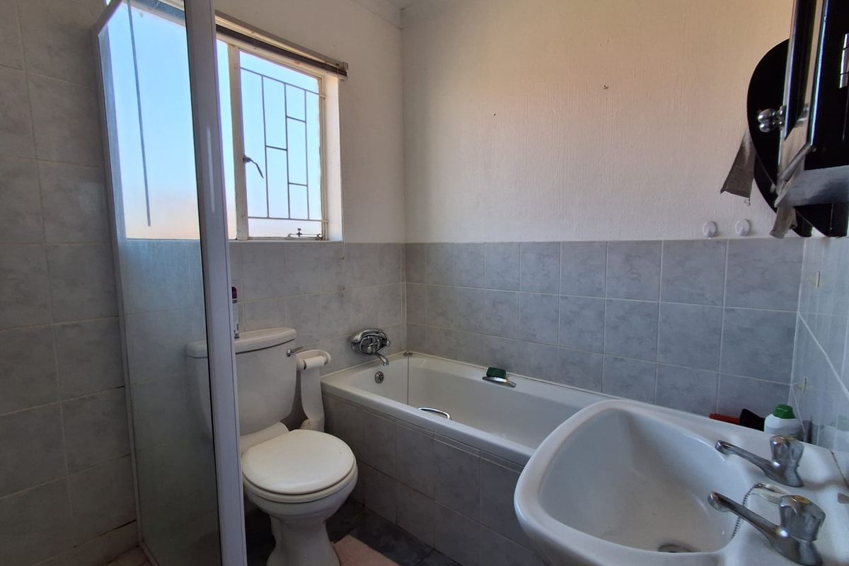 A functional bathroom featuring a built-in bathtub, a pedestal basin, and a toilet, with tiled walls and a window for natural light.