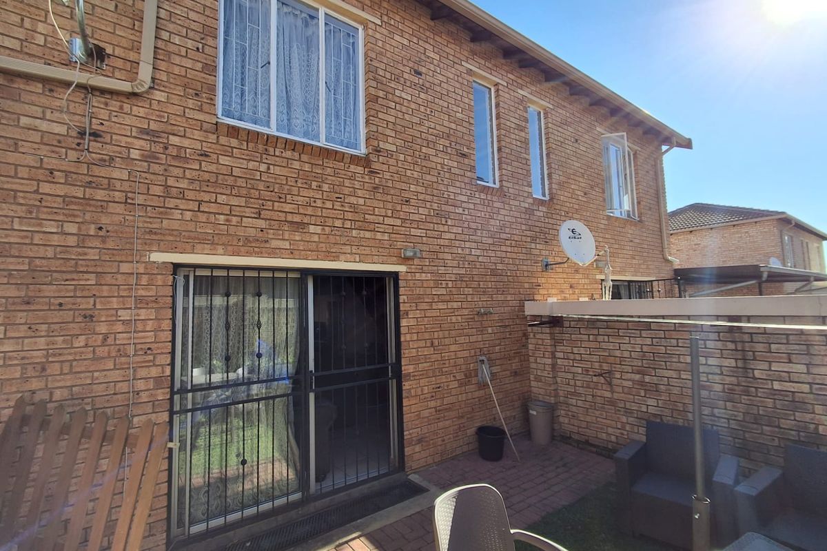 Rear view of a double-story brick townhouse featuring a paved patio area, sliding glass doors with security gates, and upper-level windows.