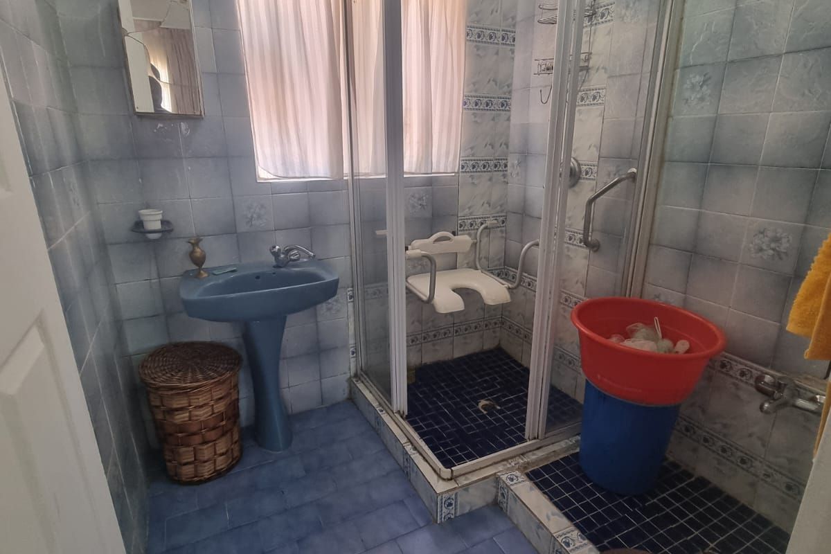 A dated bathroom featuring blue tiled walls and flooring, a pedestal basin, and a shower enclosure with integrated grab rails.
