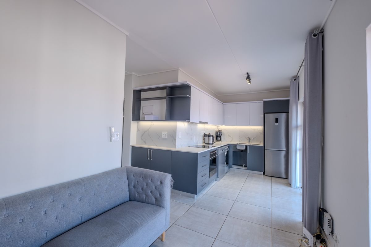 Modern open-plan kitchen featuring sleek two-tone cabinetry, marble-look splashback, integrated lighting, and tiled flooring, seamlessly flowing into the living area.