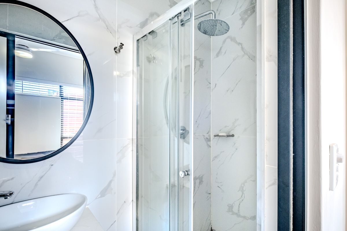 Modern bathroom featuring marble-look wall tiles, a glass-enclosed shower with a rainfall showerhead, and a contemporary vessel sink.