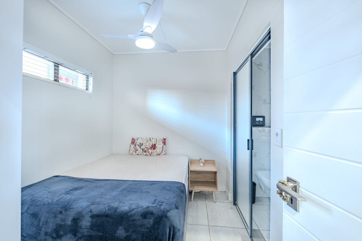 A compact bedroom featuring a ceiling fan, tiled flooring, and an en-suite bathroom with a sliding glass door.
