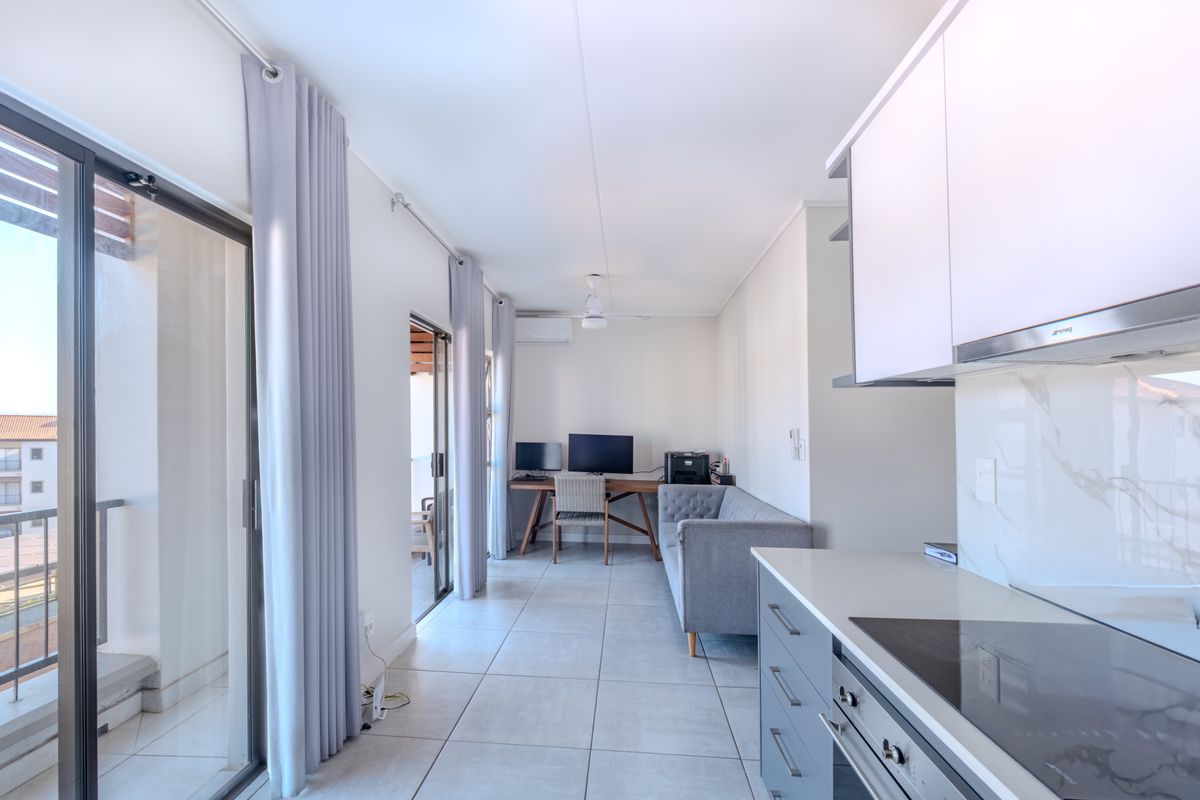 Modern open-plan living area featuring a sleek kitchen with built-in appliances, tiled flooring, and large sliding doors leading to a private balcony.