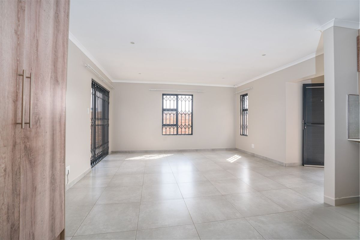 A bright, open-plan living area featuring neutral tiled flooring, recessed downlights, and secure window and door fittings.