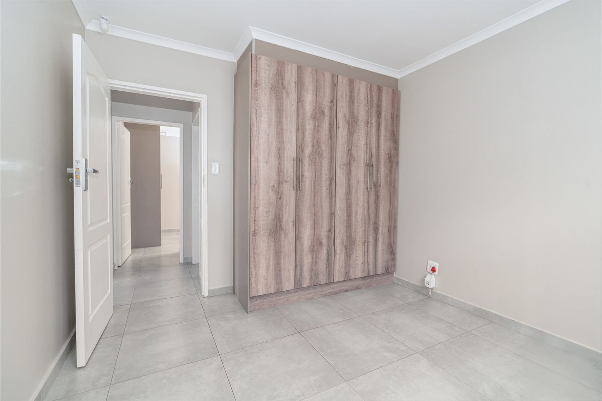 A clean, empty bedroom featuring neutral tiled flooring, a modern wood-finish built-in wardrobe, and coved ceiling detailing.