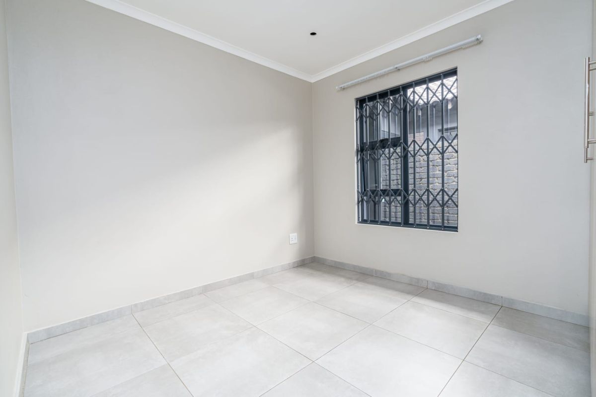 A clean, empty bedroom featuring neutral tiled flooring, light-colored walls, and a window fitted with security bars.