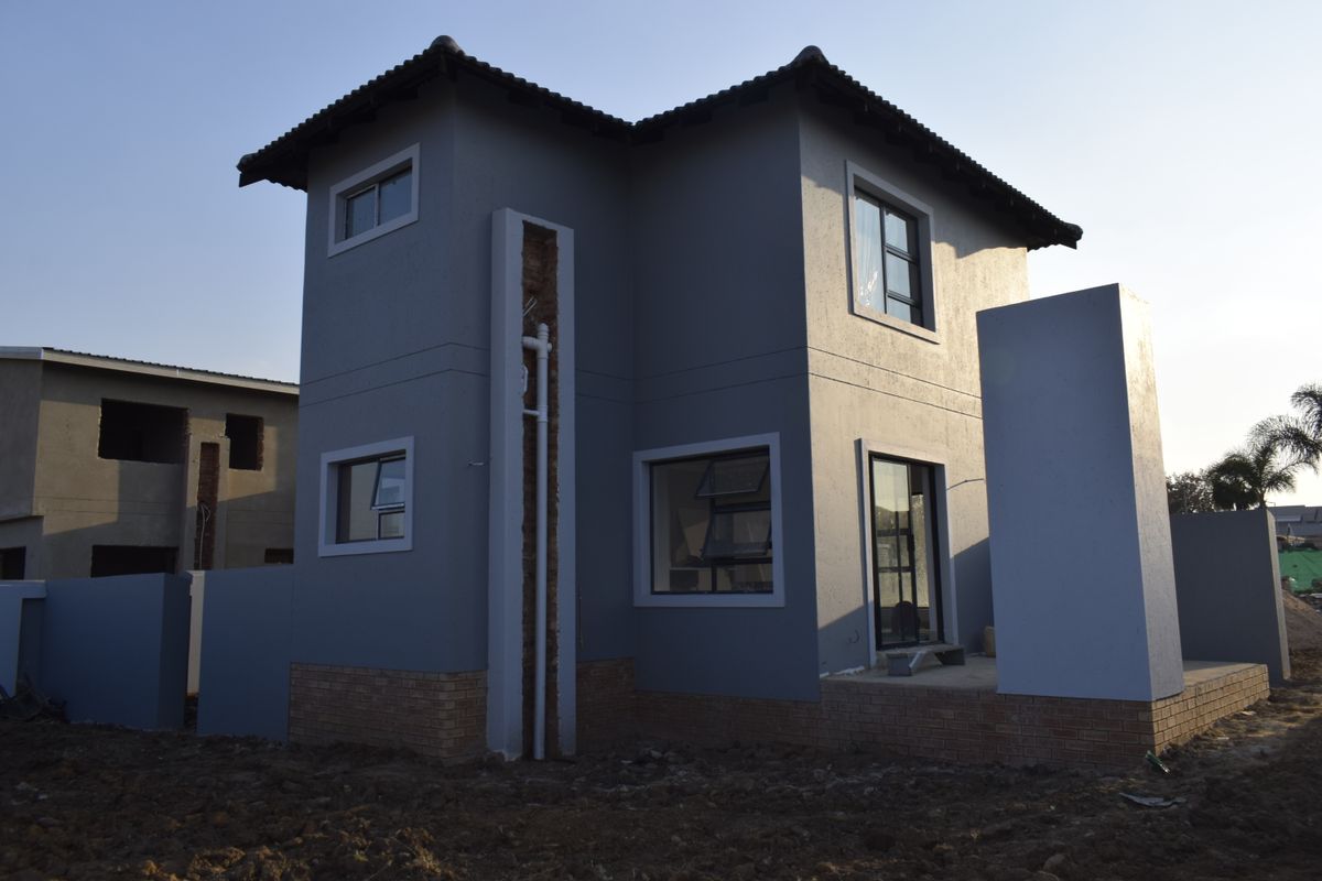 Rear view of a two-story residential house featuring a grey plastered facade, brick base, and aluminium window frames, currently in an unfinished state.