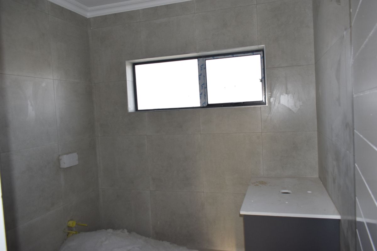 An unfinished bathroom space featuring grey wall tiles, a vanity cabinet with countertop, and exposed plumbing connections awaiting final fixture installation.