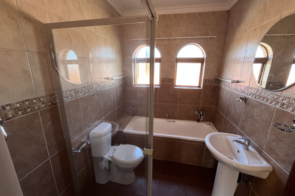 A functional bathroom featuring a pedestal basin, built-in bathtub, and a glass-enclosed shower, finished with neutral ceramic wall and floor tiles.