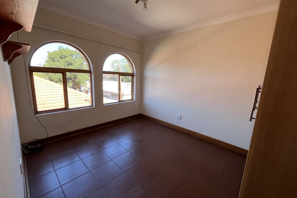 An empty bedroom featuring arched windows, tiled flooring, and neutral walls, offering a blank canvas for personalization.