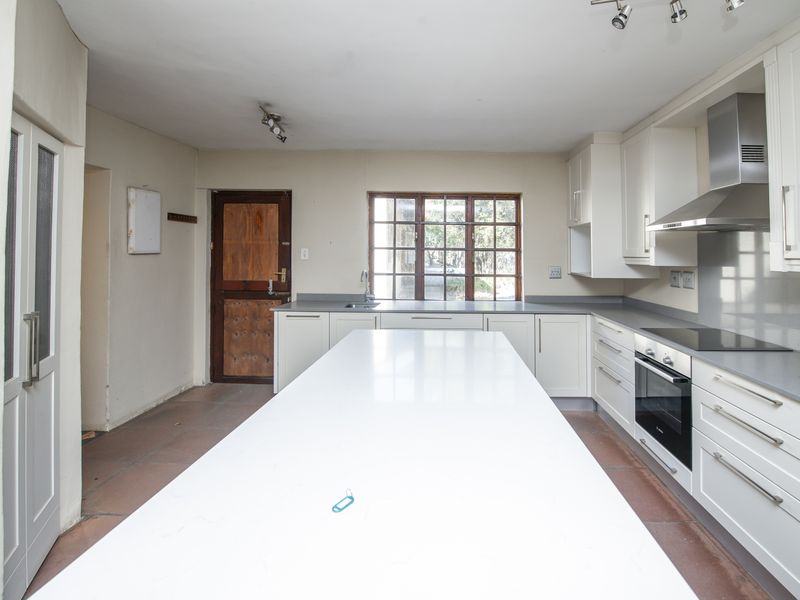 Spacious kitchen featuring a large central island, modern built-in cabinetry, integrated oven and hob, and a functional layout with direct exterior access.