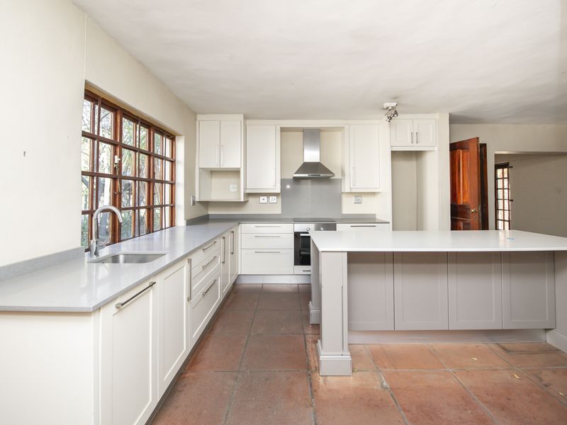 A modern, spacious kitchen featuring white cabinetry, a central island with quartz countertops, stainless steel appliances, and terracotta-style tiled flooring.