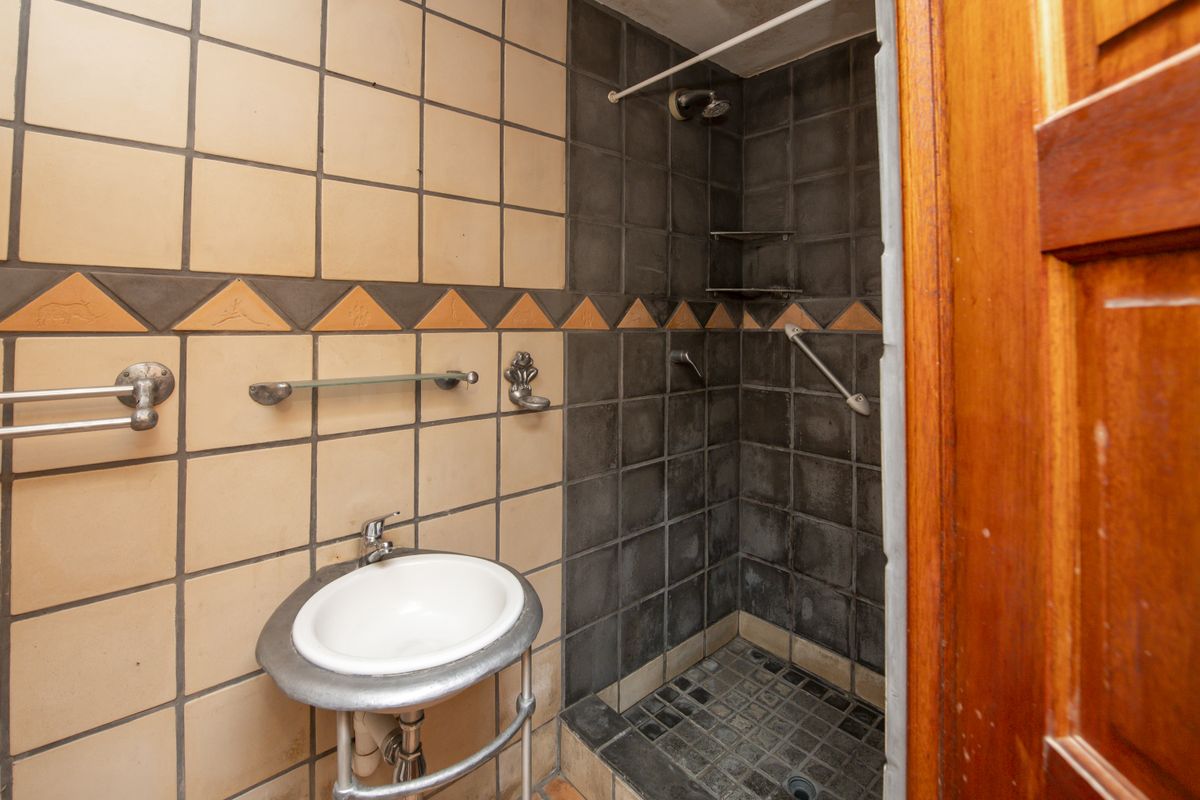A compact bathroom featuring a pedestal basin and a tiled shower enclosure with a grab rail and decorative accent tiles.