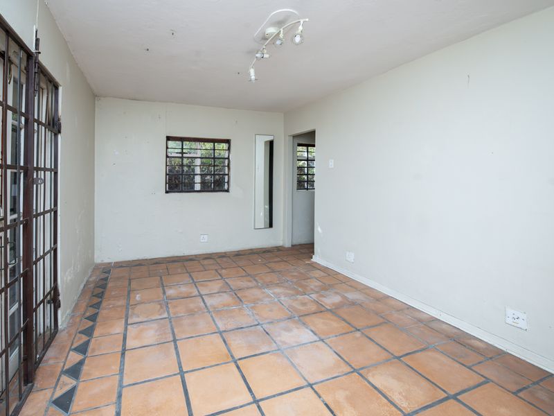 An empty living area featuring terracotta floor tiles, a security gate, and neutral walls, offering a blank canvas for renovation or staging.