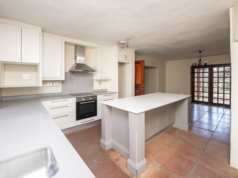 Spacious open-plan kitchen featuring a central island, modern cabinetry, built-in appliances, and terracotta flooring, leading out to a garden area.