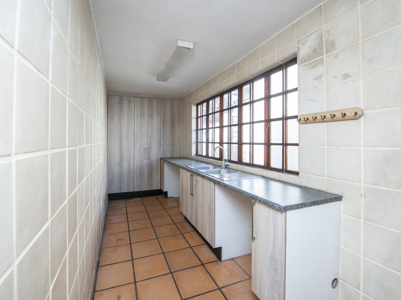 A functional scullery area featuring built-in cabinetry, a stainless steel sink, tiled walls, and terracotta floor tiles, offering ample storage and workspace.