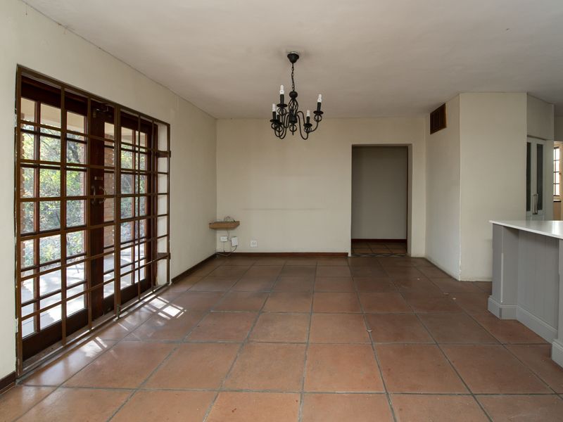 Spacious open-plan living area featuring terracotta floor tiles, a classic wrought iron chandelier, and direct access to the outdoors through secure wooden framed glass doors.