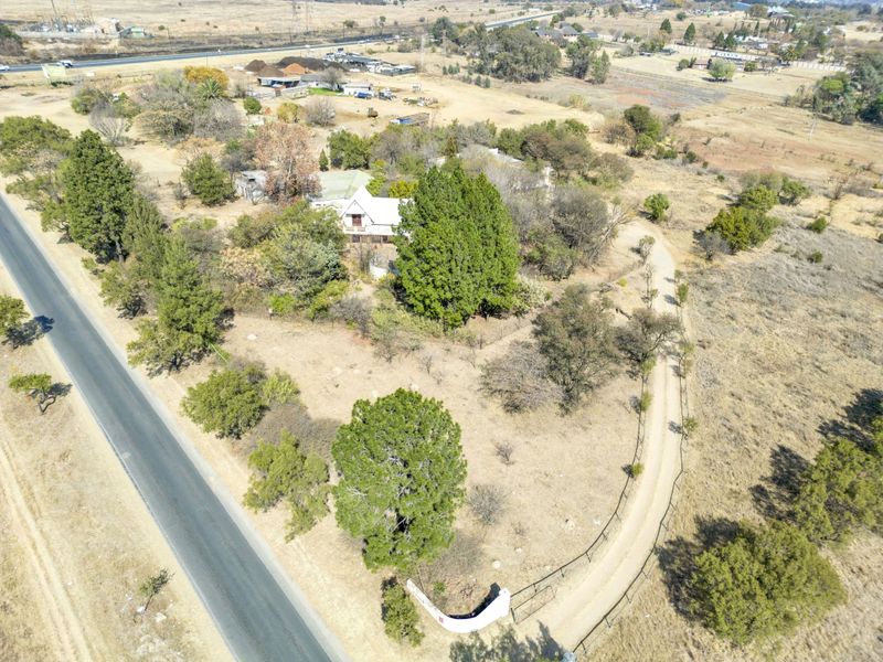 Aerial view of a small holding property featuring a gravel driveway, established trees, and perimeter fencing with direct access to the main road.
