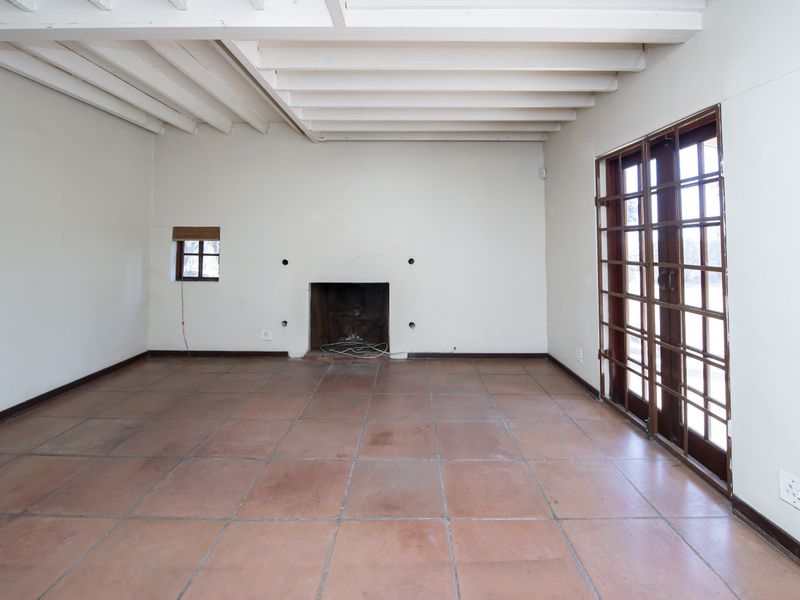 Spacious living room featuring exposed beam ceilings, terracotta floor tiles, a central fireplace, and direct access to the outdoors via wooden framed glass doors.