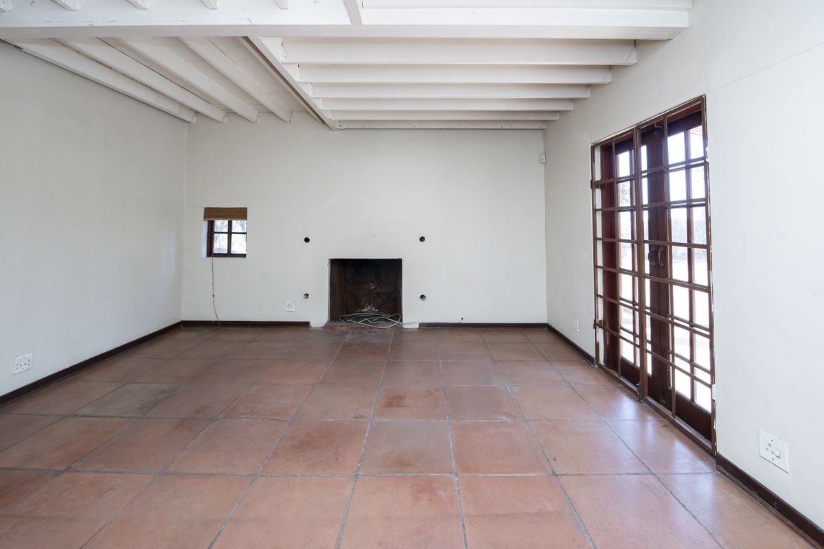 Spacious living room featuring exposed beam ceilings, terracotta floor tiles, a central fireplace, and direct access to the outdoors via wooden framed glass doors.