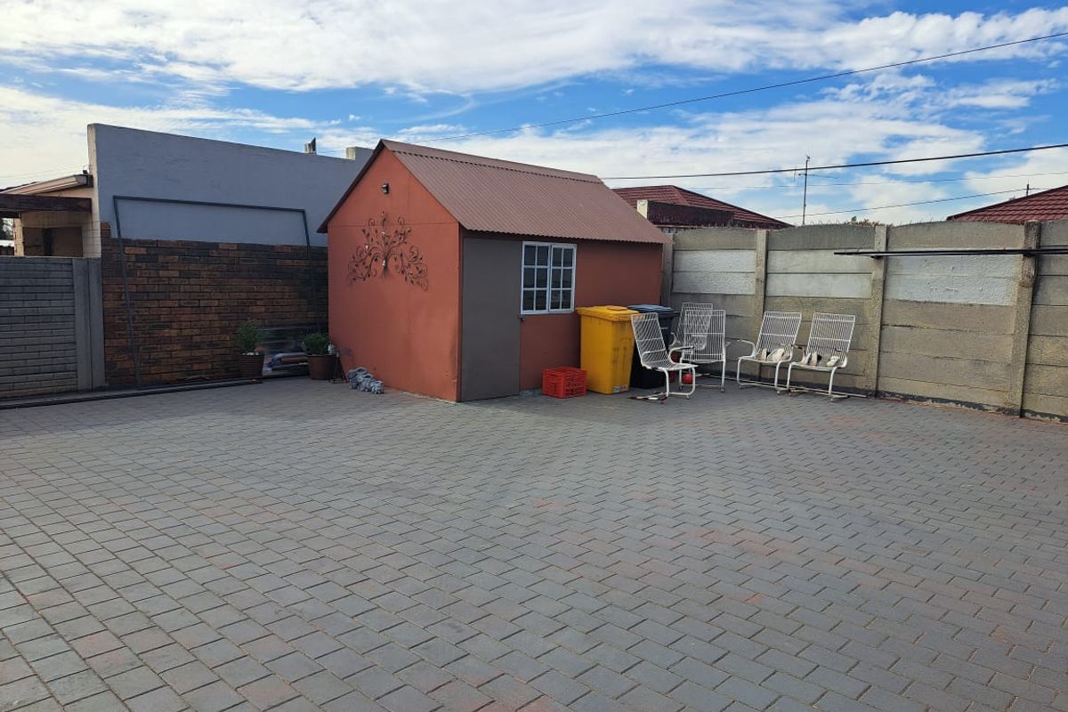 A paved rear courtyard area featuring a metal storage shed and perimeter boundary walls.
