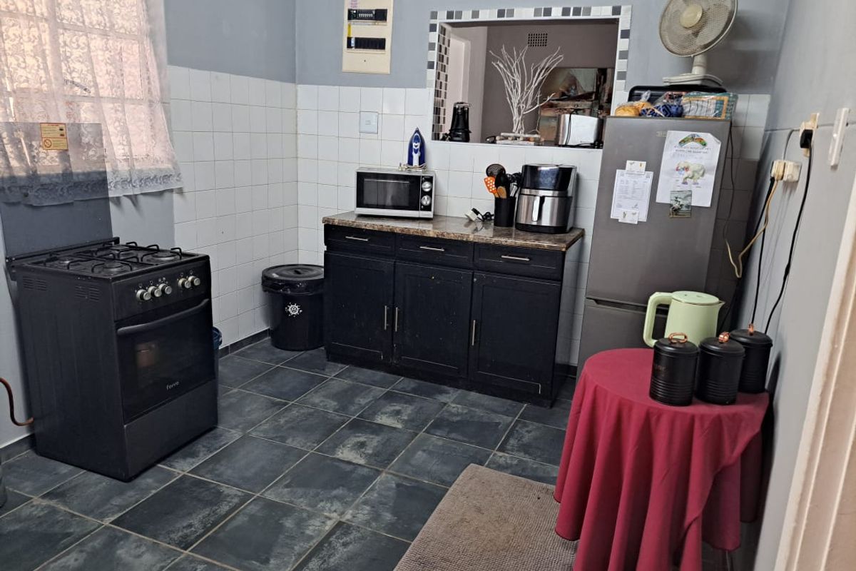 A functional kitchen featuring dark cabinetry, granite countertops, tiled splashbacks, and a convenient pass-through window connecting to the adjacent living space.