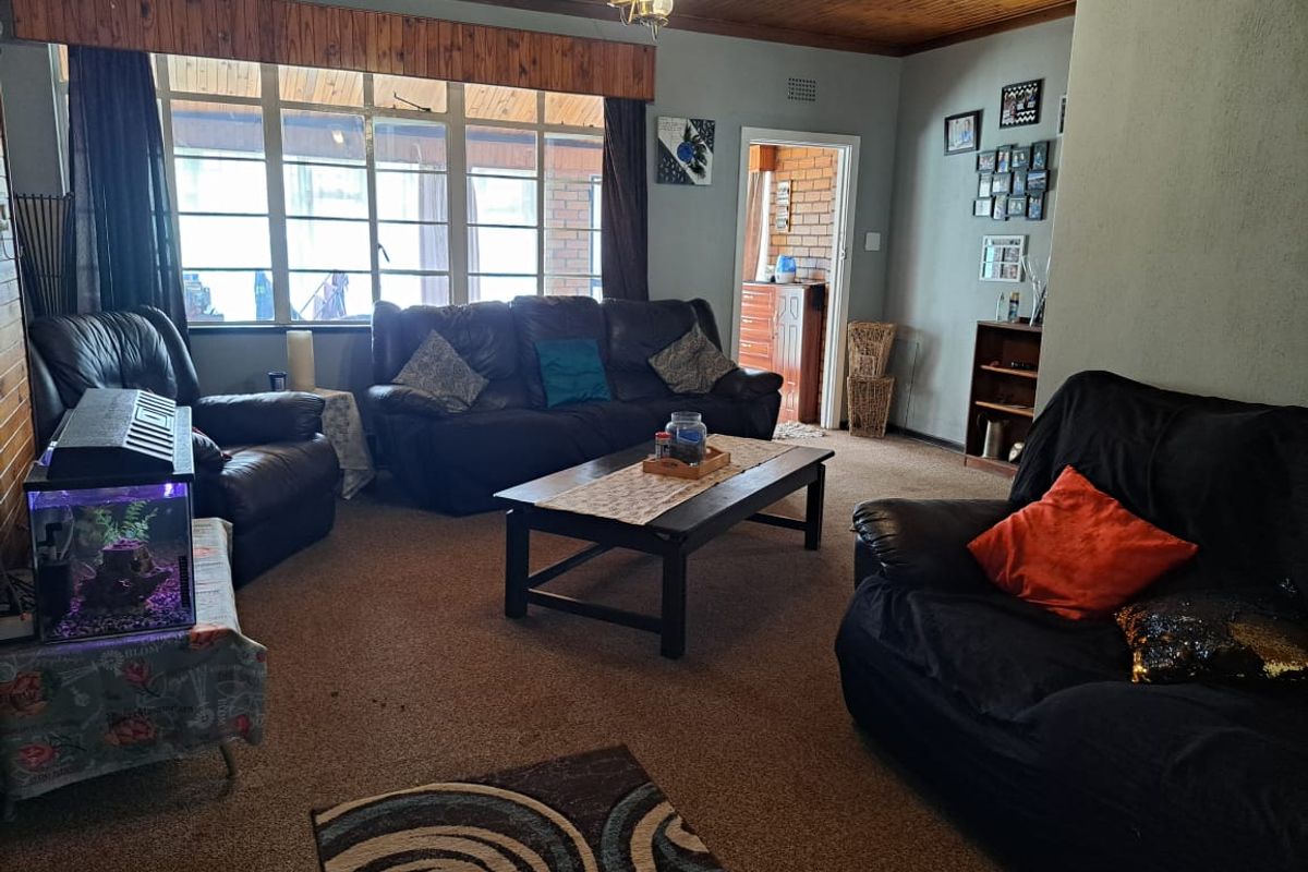 A living room featuring a timber ceiling, large windows allowing natural light, and carpet flooring, offering a comfortable and functional living space.