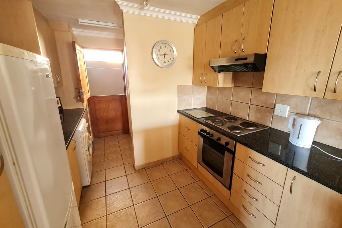 Functional kitchen featuring light wood cabinetry, granite countertops, built-in oven, electric hob, and tiled flooring with direct access to an exterior door.