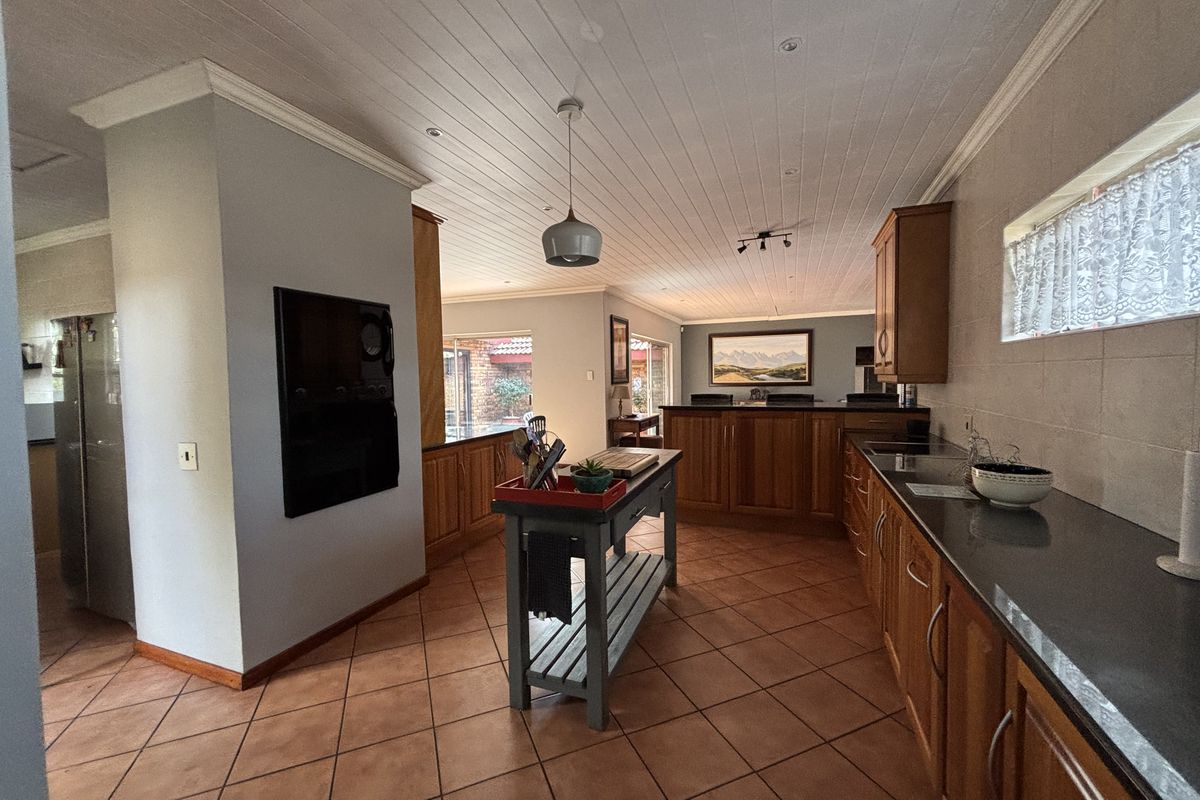 Spacious kitchen featuring warm wooden cabinetry, dark stone countertops, tiled flooring, and a classic tongue and groove ceiling with recessed lighting.
