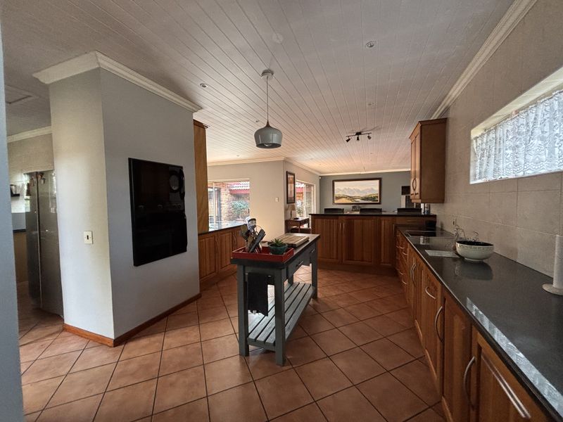 Spacious kitchen featuring warm wooden cabinetry, dark stone countertops, tiled flooring, and a classic tongue and groove ceiling with recessed lighting.