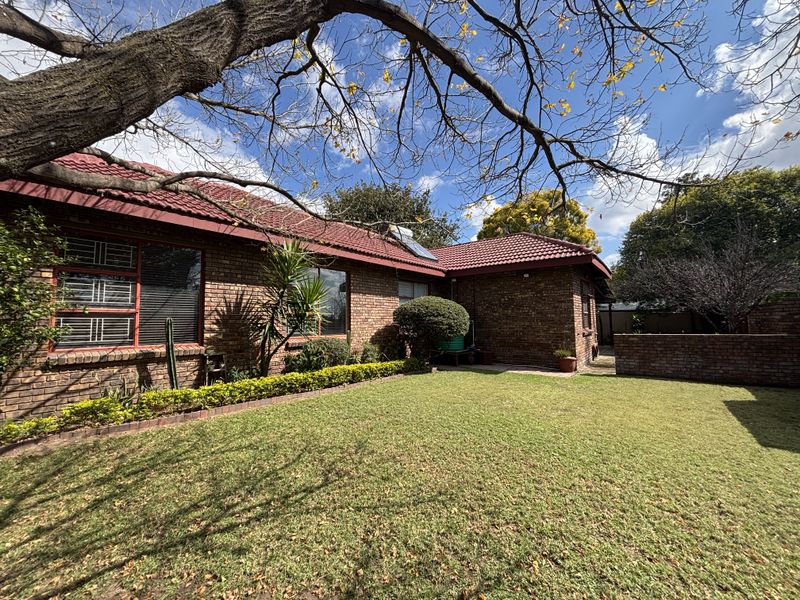 A well-maintained rear garden featuring a face brick exterior, tiled roof, and established lawn area.