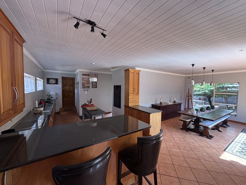 Spacious open-plan kitchen and dining area featuring granite countertops, wooden cabinetry, and ceramic tile flooring with direct access to the outdoor patio.