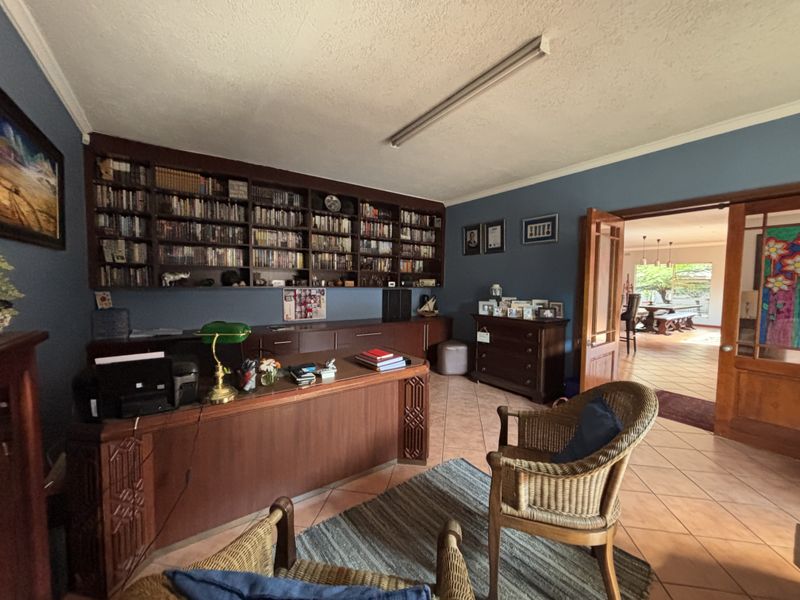Spacious home office featuring extensive built-in wooden shelving, cabinetry, and tiled flooring, with double doors leading to an adjacent living area.