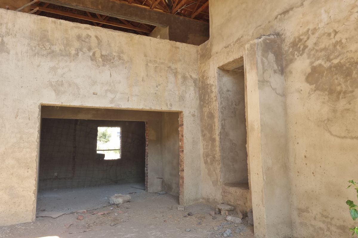 An unfinished interior space in the early stages of construction, featuring exposed timber roof trusses and raw plastered masonry walls.