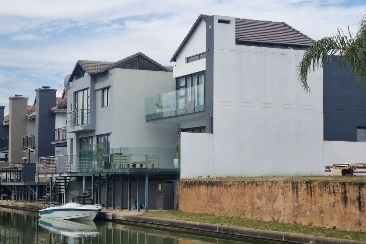 Rear view of a multi-story waterfront property featuring balconies with glass balustrades and direct canal access.