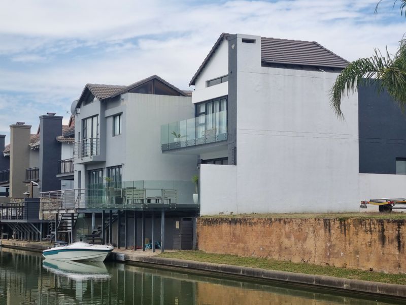 Rear view of a multi-story waterfront property featuring balconies with glass balustrades and direct canal access.